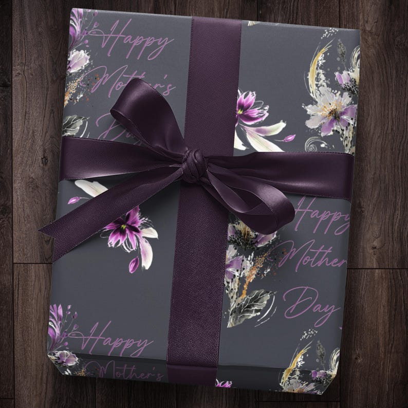 Puede incluir: Un regalo envuelto en papel de regalo gris con una cinta morada. El papel tiene un patr&oacute;n floral y el texto "Happy Mother's Day" est&aacute; impreso en &eacute;l.