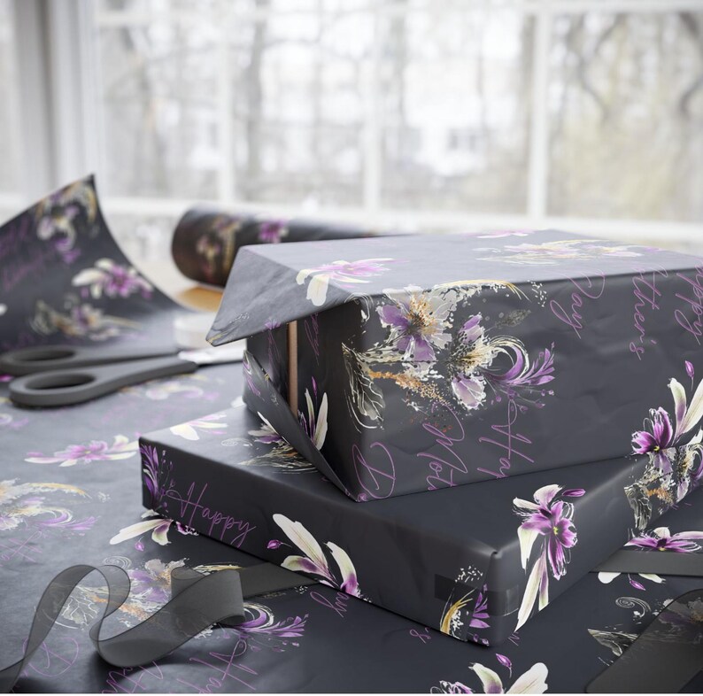 Puede incluir: Tres cajas de regalo negras envueltas en papel con estampado floral con detalles en morado y dorado. Las cajas est&aacute;n apiladas una encima de la otra. La caja superior tiene el texto "Say Hello to" escrito en ella. La caja del medio tiene el texto "It's Happy" escrito en ella. La caja inferior tiene el texto "You're" escrito en ella.
