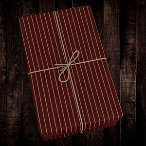 Op de afbeelding: Een rood-wit gestreepte cadeaudoos, vastgebonden met touw. De doos is ingepakt in gestreept papier met een rode achtergrond en witte strepen.