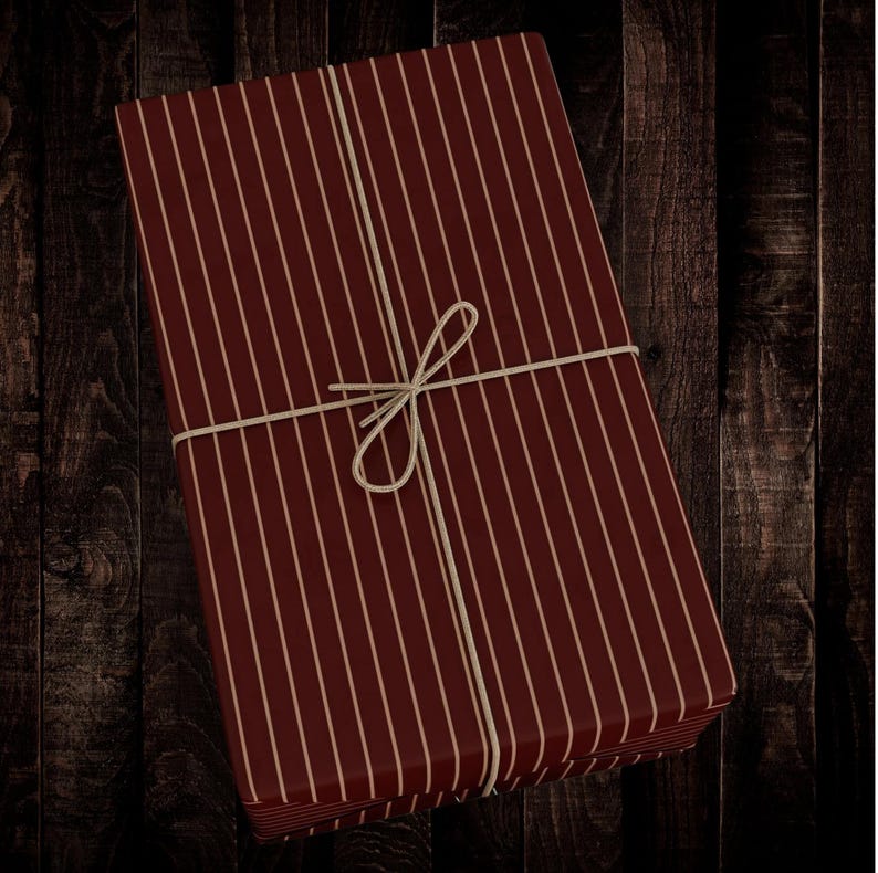Op de afbeelding: Een rood-wit gestreepte cadeaudoos, vastgebonden met touw. De doos is ingepakt in gestreept papier met een rode achtergrond en witte strepen.