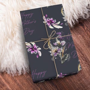 Puede incluir: Un papel de regalo azul oscuro con un patr&oacute;n floral y el texto "Happy Mother's Day" en morado. El papel est&aacute; atado con cuerda.
