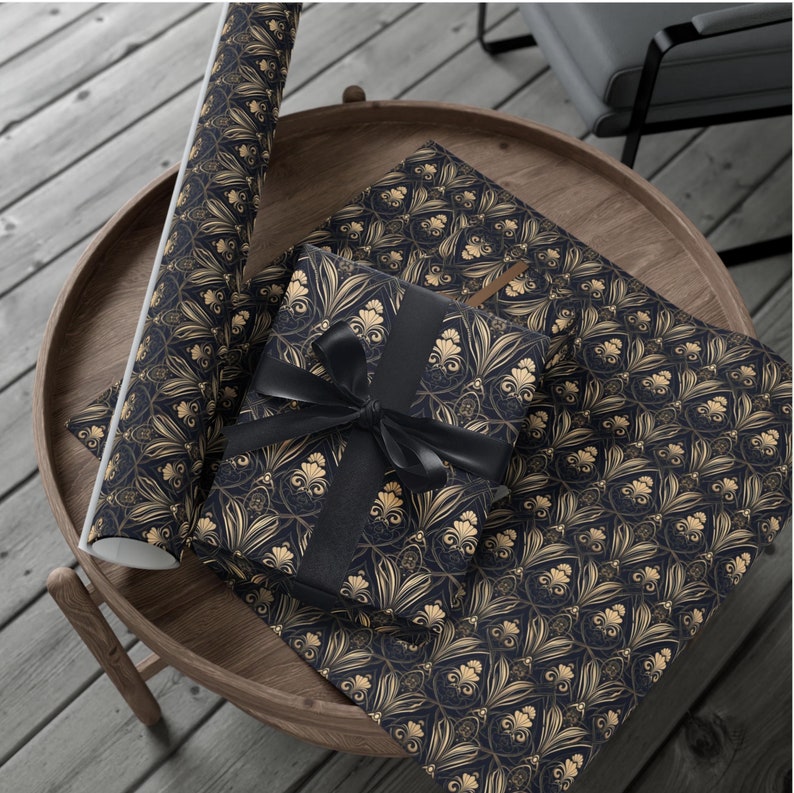 Puede incluir: Dos rollos de papel de regalo estampado en negro y dorado. Un rollo est&aacute; parcialmente desenrollado y una cinta negra est&aacute; atada alrededor.