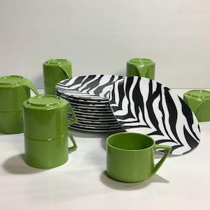 Puede incluir: Un juego de platos de cerámica verde y negro. El juego incluye cuatro tazas, cuatro platillos y un plato grande con un diseño de cebra.