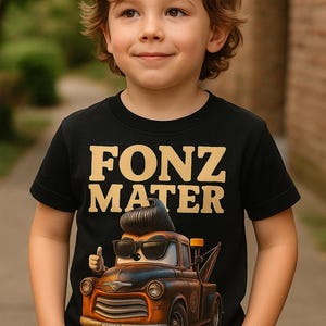 May include: A young child wearing a black t-shirt with the words "FONZ MATER" in gold lettering. The shirt features a cartoon image of a tow truck with sunglasses and a thumbs-up. The truck has the license plate "07-937".
