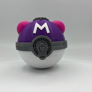 K&ouml;nnte beinhalten: Ein lila-wei&szlig;er Pok&eacute;ball mit einem rosa Knopf auf jeder Seite und einem wei&szlig;en "M" auf der Vorderseite.