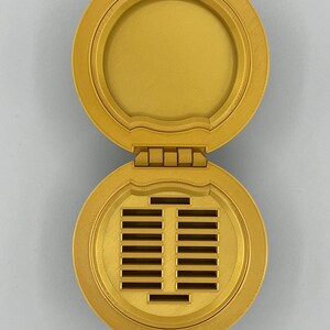K&ouml;nnte beinhalten: Eine runde, goldfarbene, Scharnierbox mit einem Raster von Schlitzen im Inneren. Die Box ist ge&ouml;ffnet und zeigt die Schlitze.