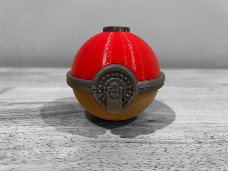 K&ouml;nnte beinhalten: Ein roter und brauner Beh&auml;lter im Pok&eacute;ball-Stil mit einem Verschluss. Der Beh&auml;lter ist aus Kunststoff und hat eine glatte, gl&auml;nzende Oberfl&auml;che.