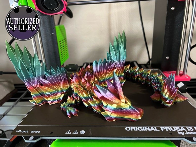 May include: A 3D-printed dragon figurine in iridescent rainbow colors. The dragon is made of geometric crystal-like shapes. The wings and body are detailed with sharp edges. The figurine is on a black surface.