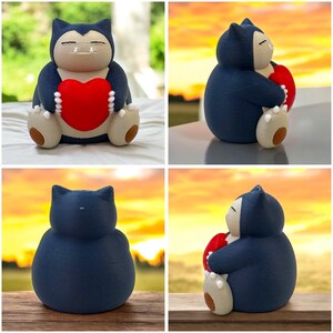Könnte beinhalten: Eine blaue und graue Pokémon-Figur, die ein rotes Herz hält. Die Figur steht auf einer Holzoberfläche.