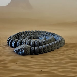 May include: A large, segmented, grey snake sculpture coiled in a circle on a sandy surface.