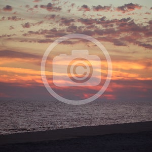 Puede incluir: Una silueta de una persona de pie en una playa de arena al atardecer. El cielo es una mezcla vibrante de naranja, rosa y morado con nubes.