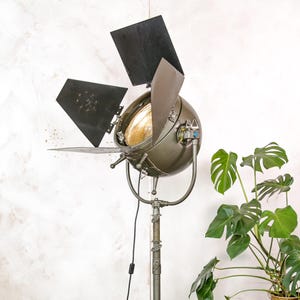 May include: A vintage green metal movie spotlight with adjustable black flaps and a round light fixture on a tall metal stand.