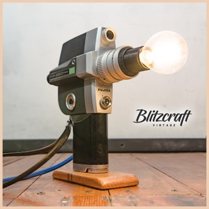 Könnte beinhalten: Eine vintage silberne und schwarze Fujica Filmkamera, die in eine Tischlampe mit einer klaren Glühbirne umgewandelt wurde. Die Kamera ist auf einem Holzsockel montiert und hat ein schwarzes Kabel.