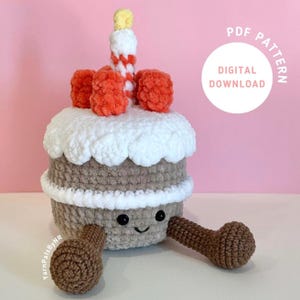 May include: Crochet pattern for a brown and white cake with red and white frosting and a yellow and red candle. The cake has two brown arms and a smiling face. The pattern is a digital download. "PDF PATTERN DIGITAL DOWNLOAD" is written in a white circle on a pink background.