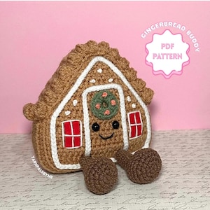 May include: A crocheted gingerbread house with a smiling face, red window details, and a green wreath. The house has brown and white accents, and the text "Gingerbread Buddy PDF Pattern" is visible.