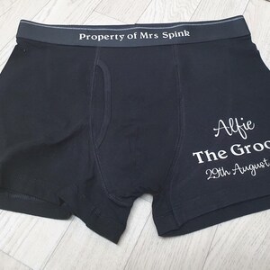 May include: Dark navy boxer shorts with the text "Property of Mrs Spink" on the waistband. The right leg features the name "Alfie", the words "The Groom", and the date "29th August 2021" in white script.