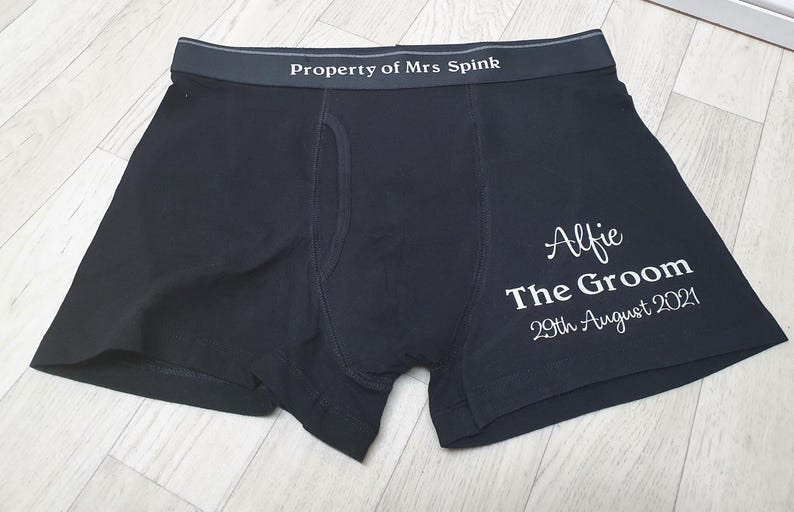 May include: Dark navy boxer shorts with the text "Property of Mrs Spink" on the waistband. The right leg features the name "Alfie", the words "The Groom", and the date "29th August 2021" in white script.