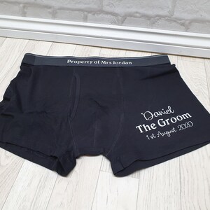 May include: Black boxer shorts with the text "Property of Mrs Jordan" on the waistband. The right leg features the text "Daniel The Groom 1st August 2020" in white script. The garment is made of a soft material.