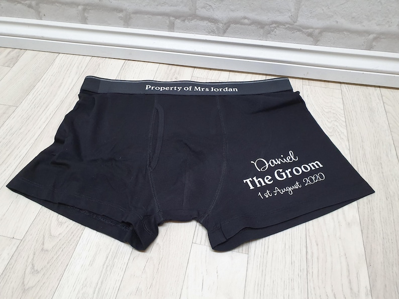 May include: Black boxer shorts with the text "Property of Mrs Jordan" on the waistband. The right leg features the text "Daniel The Groom 1st August 2020" in white script. The garment is made of a soft material.