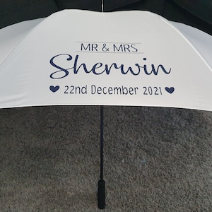 May include: White wedding umbrella with black text that reads "MR & MRS Sherwin 22nd December 2021" with a heart on each side of the date.
