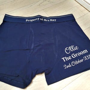 May include: Dark blue boxer shorts with white text. The waistband reads "Property of Mrs May". The right leg has the text "Ollie The Groom 2nd October 2020".