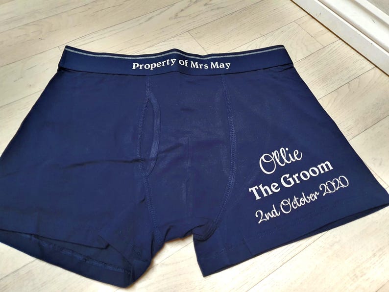 May include: Dark blue boxer shorts with white text. The waistband reads "Property of Mrs May". The right leg has the text "Ollie The Groom 2nd October 2020".