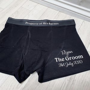 May include: Black boxer shorts with the text "Property of Mrs Barnes" on the waistband. The right leg has the text "Ryan The Groom 31st July 2020" in white script. The underwear is made of a soft material.