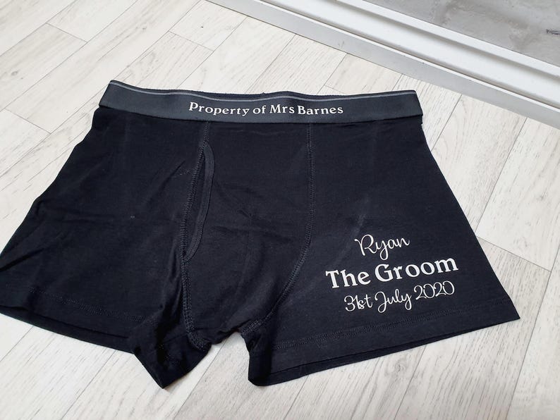 May include: Black boxer shorts with the text "Property of Mrs Barnes" on the waistband. The right leg has the text "Ryan The Groom 31st July 2020" in white script. The underwear is made of a soft material.
