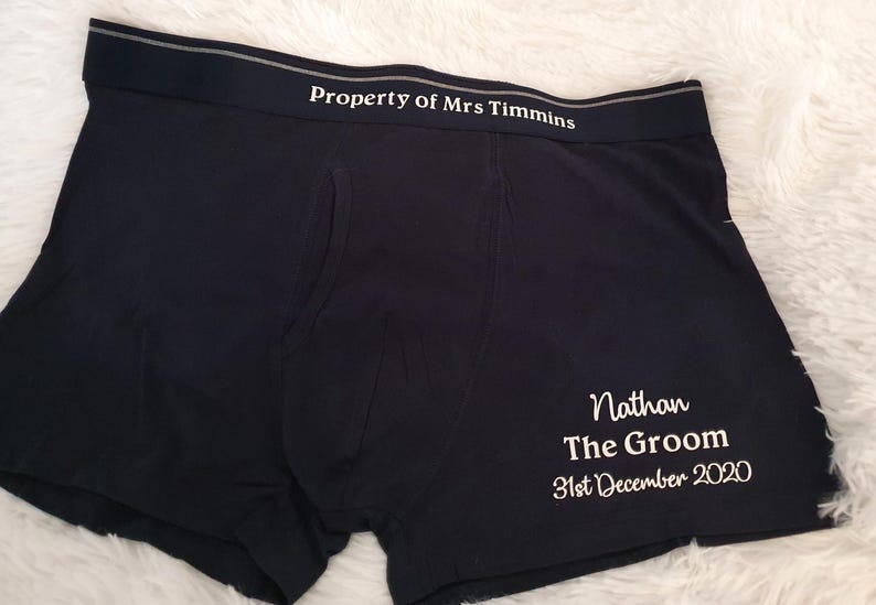 May include: Black boxer shorts with the text "Property of Mrs Timmins" printed on the waistband. The text "Nathan The Groom 31st December 2020" is printed on the leg of the underwear. The underwear is made of a soft material.