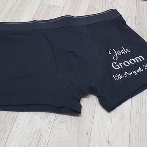 May include: Black boxer shorts with the text "Josh Groom 15th August 2020" in white script. The underwear features a comfortable waistband and a classic design. Ideal for a wedding or special event.