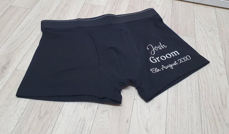 May include: Black boxer shorts with the text "Josh Groom 15th August 2020" in white script. The underwear features a comfortable waistband and a classic design. Ideal for a wedding or special event.
