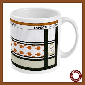Puede incluir: Taza de cerámica blanca con un gráfico de la entrada de una estación de metro de Londres. El nombre de la estación "Lambeth North" está impreso en negro sobre una franja naranja. El gráfico presenta una pared de azulejos con acentos naranja y negro, un suelo de azulejos blanco y negro y un letrero de "Way Out".