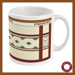 Puede incluir: Taza de cerámica blanca con un gráfico de la estación de metro Embankment en Londres. El gráfico presenta una pared de ladrillo rojo con un patrón de azulejos verdes y blancos y un letrero que dice "Way Out".