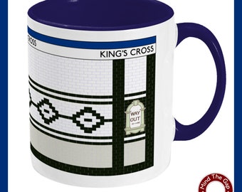 May include: White ceramic mug with a blue rim and handle. The mug features a graphic of a London Underground station sign with the text "KING'S CROSS" and a black and white tiled pattern. The sign also includes the text "WAY OUT" with an arrow.