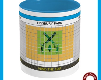 May include: White ceramic mug with a blue rim. The mug features a graphic of a London Underground station sign with the text "Finsbury Park" and a stylized image of crossed pistols with a tree in the center. The text "Mind the Gap" is printed below the graphic.