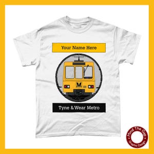 May include: White t-shirt with a yellow Tyne & Wear Metro train illustration. The design includes the text "Your Name Here" above the train and "Tyne & Wear Metro" below. A graphic design logo is in the bottom right corner.