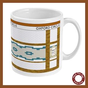 Puede incluir: Taza de cerámica blanca con un gráfico de una plataforma de estación de metro de Londres. El nombre de la estación "Oxford Circus" está impreso en naranja sobre un fondo marrón. La plataforma tiene azulejos blancos con acentos marrones y azules. Un letrero dice "Way Out" con una flecha apuntando hacia la derecha.