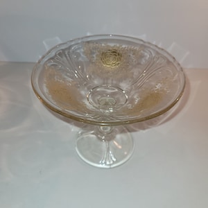 Könnte beinhalten: Eine klare Glasschale auf einem Sockel mit goldenem Blumendesign. Die Schale hat einen gewellten Rand und einen Fuß.