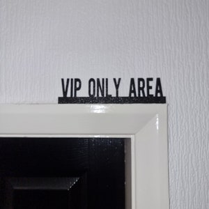 Op de afbeelding: Een wit deurkozijn met een zwart bord met de tekst "VIP ONLY AREA" erboven.
