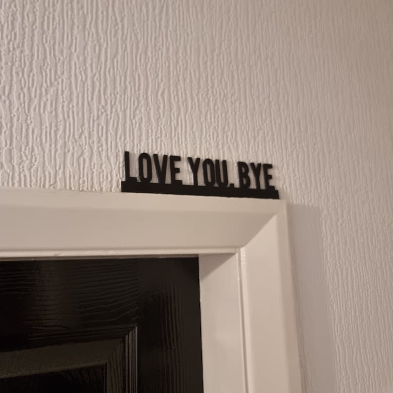Op de afbeelding: Zwart deurschild met de tekst "LOVE YOU. BYE" in witte letters.