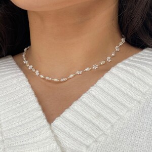 May include: A delicate white pearl and flower choker necklace. The necklace is made of small white pearls and tiny white flower charms.