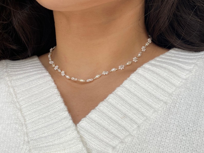 May include: A delicate white pearl and flower choker necklace. The necklace is made of small white pearls and tiny white flower charms.