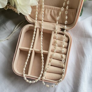 May include: A pink velvet-lined jewelry box with two pearl necklaces inside. One necklace is made of small white pearls and the other is made of larger white pearls.