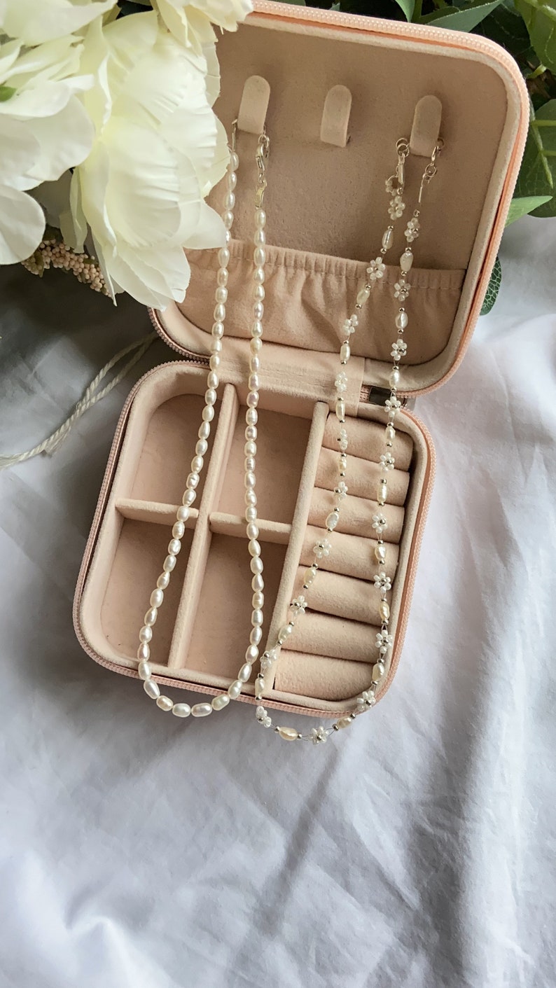 May include: A pink velvet-lined jewelry box with two pearl necklaces inside. One necklace is made of small white pearls and the other is made of larger white pearls.