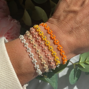 May include: Five beaded bracelets with flower-shaped beads in shades of white, cream, peach, yellow and orange.