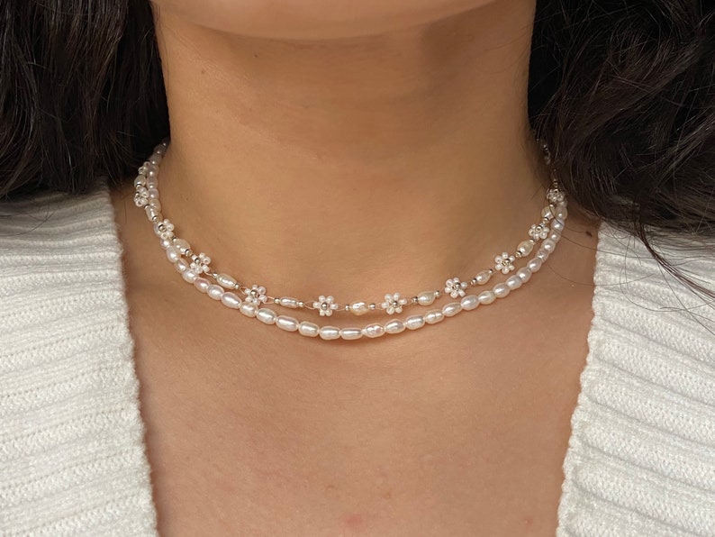 May include: A delicate double-strand pearl necklace with small white flower accents. The necklace is made of white pearls and silver.