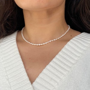 May include: A simple white pearl necklace with a delicate design. The necklace is made of small, round pearls that are strung together on a thin chain. The necklace is perfect for adding a touch of elegance to any outfit.