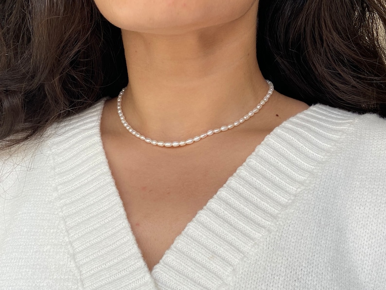May include: A simple white pearl necklace with a delicate design. The necklace is made of small, round pearls that are strung together on a thin chain. The necklace is perfect for adding a touch of elegance to any outfit.