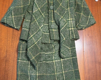 May include: A green and white plaid skirt suit with a short-sleeved jacket. The jacket has a shawl collar and two buttons. The skirt is knee-length.