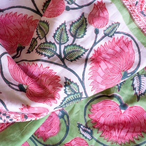 May include: Close-up of floral fabric with a repeating pattern of pink flowers and green leaves on a white and green background. The fabric is folded, showing the detailed design.